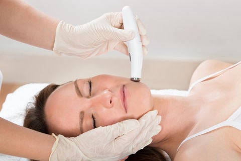A professional in cream gloves using a white microdermabrasion wand to perform an exfoliation treatment on a client's jawline