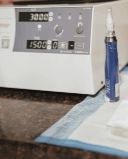 Clinical setup for PRP Microneedling featuring a tabletop centrifuge machine with digital displays for RCF and time, positioned next to a blue SkinPen microneedling device on a sterile drape