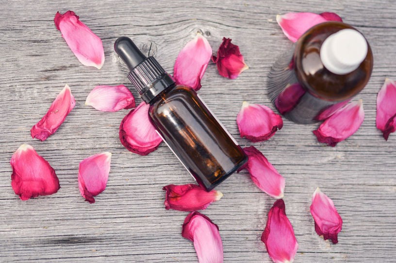 Amber glass skincare dropper bottle surrounded by pink rose petals on a wooden surface